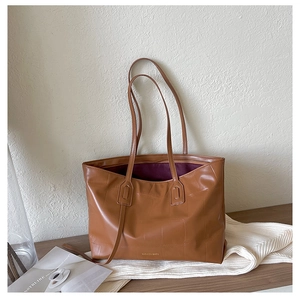 Detail of crocodile-embossed brown leather tote showing the wide base and brand lettering