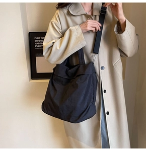 Seitenansicht einer schwarzen Nylon-Tasche mit breitem Gurt auf khakifarbenem Trenchcoat