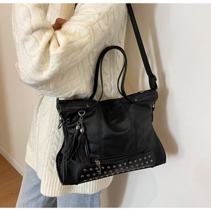 Detail of black pebbled leather tote bag featuring silver studs and leather tassel charm
