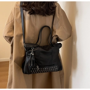 Detail of black tote bag with vintage tassels and metallic studs on a khaki trench coat