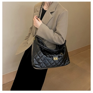 Detail of black quilted shoulder bag featuring gold twist lock and chain strap on model