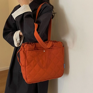 Deep orange quilted tote bag with diamond stitching and drawstring closure shown on model