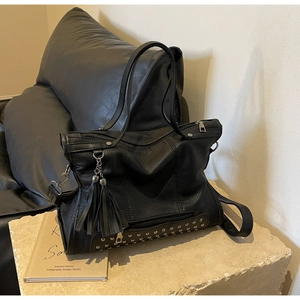 Detail shot of black leather tote bag with metallic rivets and long side tassels
