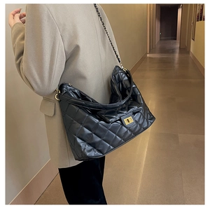 Classic black quilted tote bag with gold chain strap worn over a khaki blazer