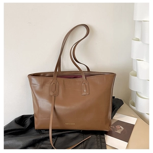 Close-up of brown tote bag featuring faux crocodile texture and gold fashion logo