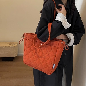 Orange quilted diamond tote bag with side drawstrings and top handles in a minimalist setting