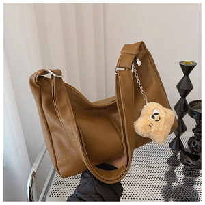Brown faux leather tote bag with wide shoulder strap and beige plush bear pendant
