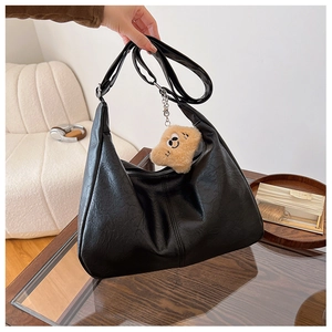 Macro detail of black hobo bag's matte leather texture with a cute plush bear charm
