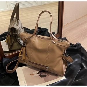Detail of khaki pebbled leather tote bag with metallic rivets and tassel charm