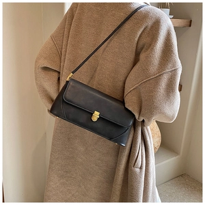 Grand sac porté épaule vintage noir avec boucle dorée sur un manteau en laine