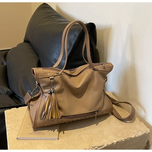 Close-up of khaki tote bag featuring rivet details, tassels and pebbled faux leather texture
