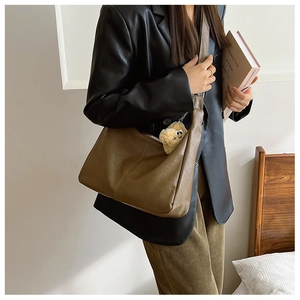 Detail of dark brown matte leather tote bag with yellow plush bear charm and wide strap