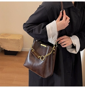 Detail of vintage brown bucket bag with gold chain strap and polished leather texture