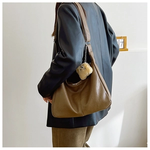Brown faux leather hobo bag with teddy bear pendant worn by a model in a minimal setting