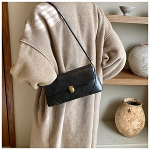 Détail d'un sac sous le bras en cuir noir vintage avec un fermoir doré sur un manteau de laine