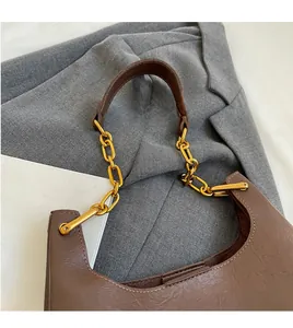 Détail du sac bandoulière en cuir marron foncé avec chaîne dorée sur un blazer gris