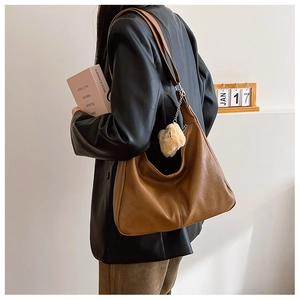 Close-up of brown faux leather hobo bag with plush ball charm and wide strap detail