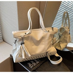 Detail of white lychee leather tote bag featuring decorative tassels and metal rivets