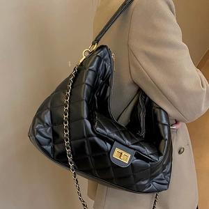 Quilted black leather tote bag with metal chain strap shown on model in khaki suit