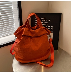 Detail einer orangefarbenen Nylon-Tragetasche mit Faltenstruktur und Stoffschultergurt
