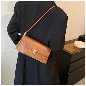 Détail d'un sac à bandoulière marron vintage avec fermoir doré sur blazer noir