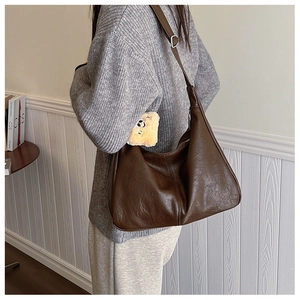 Detail of dark brown leather tote bag with vintage texture and plush bear accessory