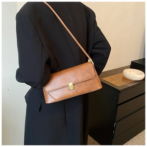 Détail du sac sous le bras en cuir marron vintage avec boucle dorée sur veste noire
