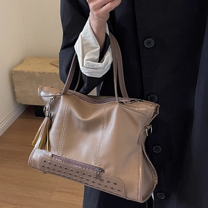 Khaki brown leather tote bag with silver rivets and tassel detail held by model