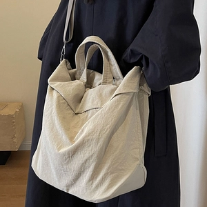 Große beige Nylon-Eimertasche getragen mit dunklem Mantel für einen Herbst-Look