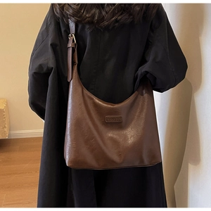 Détail du sac hobo en cuir marron foncé avec bandoulière réglable et logo embossé