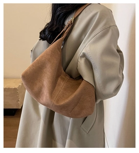 Side view of brown suede hobo bag with topstitching worn with a beige trench coat