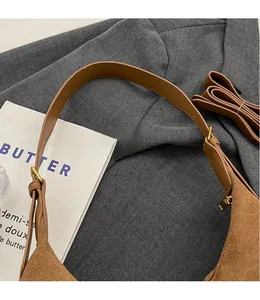 Detail of a brown frosted suede crescent bag with smooth straps and golden hardware