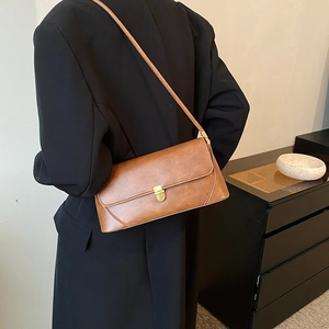 Sac à épaule vintage marron avec fermoir doré porté sur une veste de blazer noire