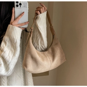Detail shot of a beige frosted suede half-moon shoulder bag worn by a model in knitwear
