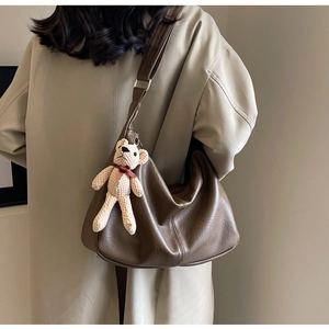 Detalle del bolso tote de cuero marrón oscuro con colgante de oso de punto y hebilla dorada