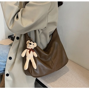 Detalle del bolso tote grande de cuero marrón con un pequeño colgante de oso de peluche