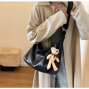 Detalle de bolso tote de cuero sintético negro con textura suave y colgante de oso