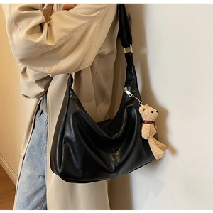 Detalle del bolso media luna de cuero negro con correa ajustable y colgante de oso
