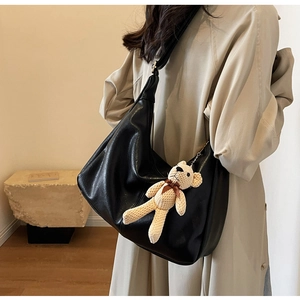 Detalle de bolso hobo de cuero negro con colgante de osito llevado por una modelo