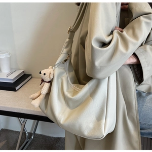Detalle de un bolso tote crema grande con un colgante de oso tejido sobre cuero PU suave