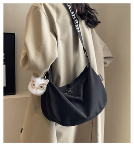 Detail of black nylon moon bag featuring fashion strap and owl charm on a trench coat