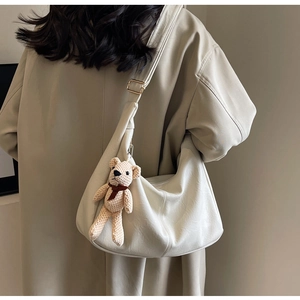 Detalle de bolso hobo crema con correa ajustable y colgante de osito de punto suave
