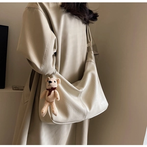 Detalle lateral de bolso tote grande beige con colgante de oso tejido y correa larga