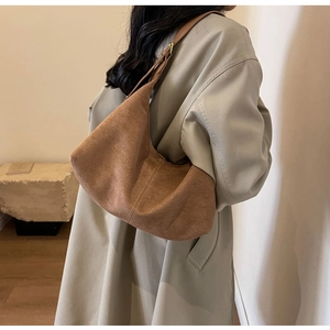Detailed side view of a brown vintage matte suede crescent bag worn with a beige coat