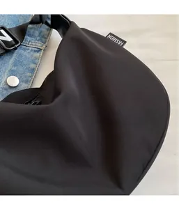 Close-up of black nylon half-moon crossbody bag with Fashion label on denim background