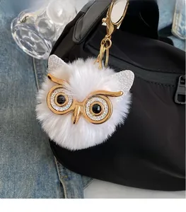 Detail of a white fluffy owl pendant with gold glasses attached to a black nylon bag