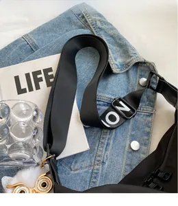 Detail of black nylon crossbody bag with owl charm and logo strap on denim fabric