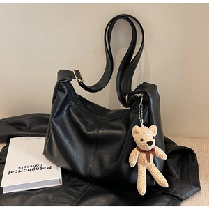 Detalle del bolso tote negro de cuero con un tierno colgante de oso tejido beige