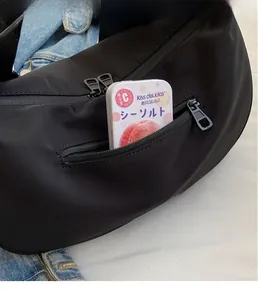 Detail of front zipper pocket on black nylon crossbody bag showing storage capacity