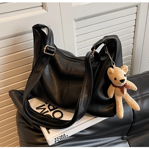 Detalle de bolso tote de cuero granulado negro con herrajes dorados y oso de ganchillo